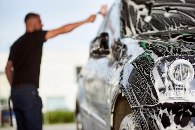 Sportlicher Mann, der sein schwarzes Auto draußen wäscht