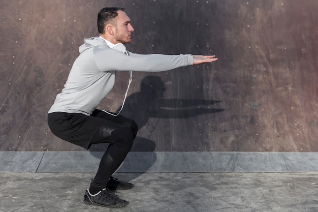 Sportlicher Mann der Seitenansicht, der Hocken tut