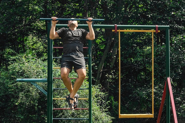 Sportlicher Mann führt Klimmzugübungen am Reck im Kinderaußenbereich durch