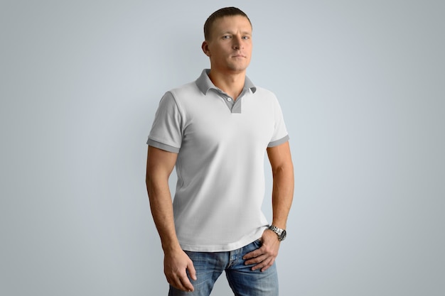 Sportlicher Mann im leeren Polohemd und in der blauen Jeans mit der Hand in der Tasche einzeln auf der grauen Wand, abgewinkelte Vorderansicht.