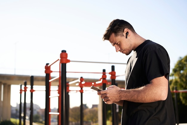 Sportlicher Mann in einem Barpark unter Verwendung seines Smartphones während des Calisthenics-Trainings im Freien.