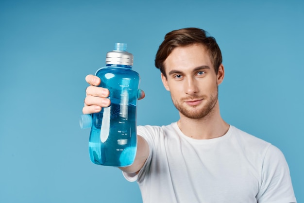 Sportlicher Mann in weißem T-Shirt hält eine blaue Wasserflasche vor seinem Studio. Hochwertiges Foto