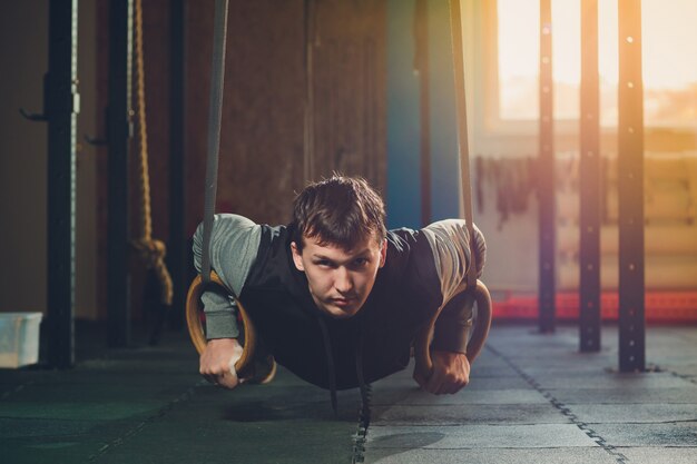 Sportlicher Mann mit Muskelaufbau, der intensives Training im Fitnessstudio auf Turnringen durchführt.