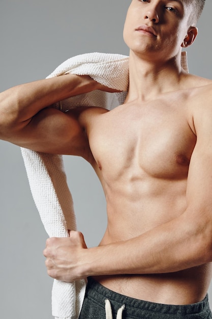 Sportlicher Mann mit muskulösem Rumpf, Handtücher in den Händen, abgeschnittener Blick, grauer Hintergrund, hochwertiges Foto
