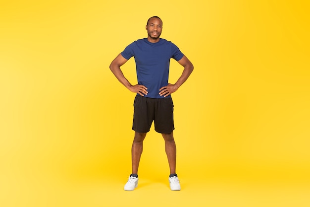 Foto sportlicher schwarzer mann, der die hände auf den hüften hält, die auf gelbem hintergrund stehen
