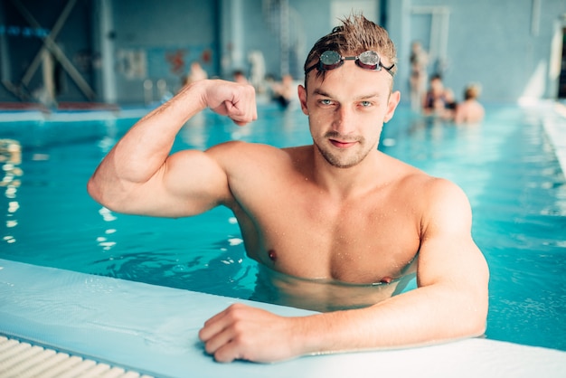 Sportlicher Schwimmer zeigt Muskeln, Hallenbad.