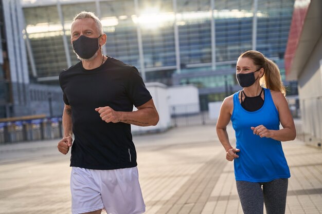 Sportliches Ehepaar mittleren Alters, das morgens mit Schutzmasken joggt, covid verantwortliches Verhalten