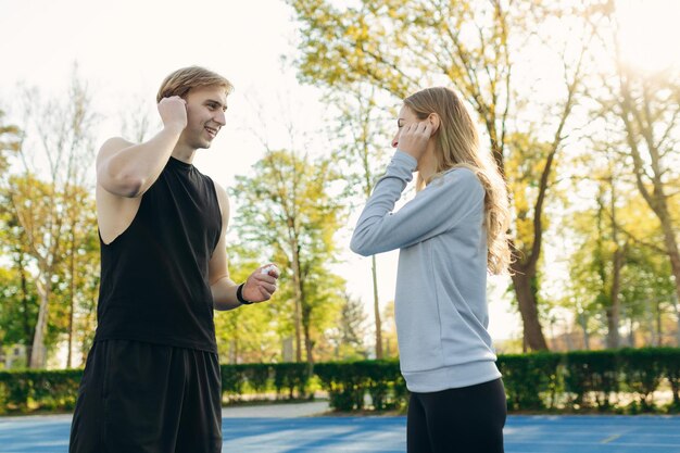 Sportliches junges Paar im Stadion, das miteinander spricht Der Typ und das Mädchen bereiten sich auf das gemeinsame Training vor Das Konzept eines gesunden Lebensstils