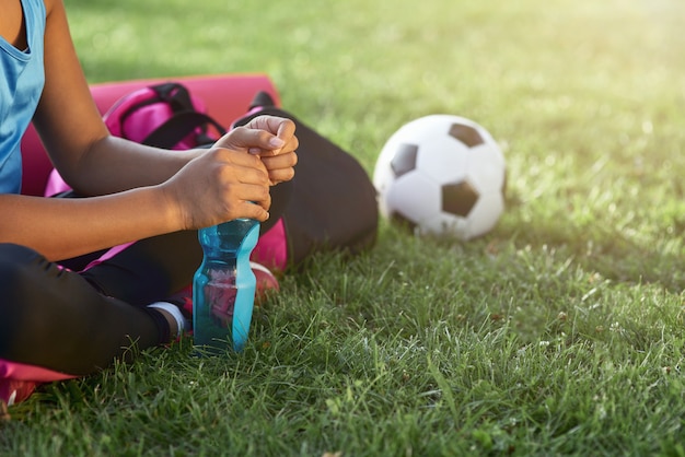 Sportliches kleines Mädchen mit einer Flasche Wasser, das auf Gras sitzt