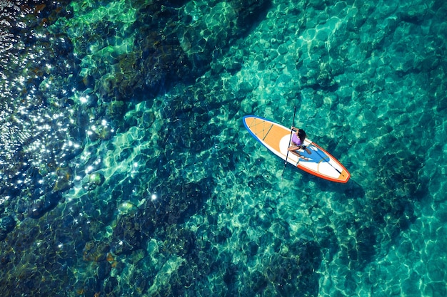 Sportliches Mädchen, das beim Sitzen in einem rosa Bikini auf einem Surfbrett aufwirft