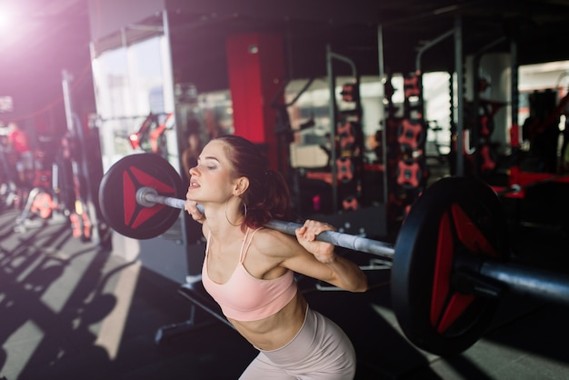 Sportliches Mädchen in Sportbekleidung macht Übungen mit einer Langhantel, Hanteln. Fitness, Training, gesunder Lebensstil