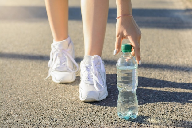 Sportliches Mädchen in weißen Turnschuhen hielt auf der Straße an, um eine Pause einzulegen und etwas Wasser zu trinken