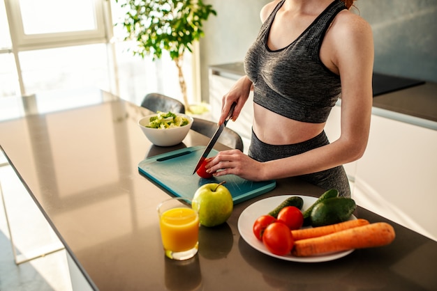 Sportliches Mädchen mit Sportkleidung isst einen Salat in der Küche