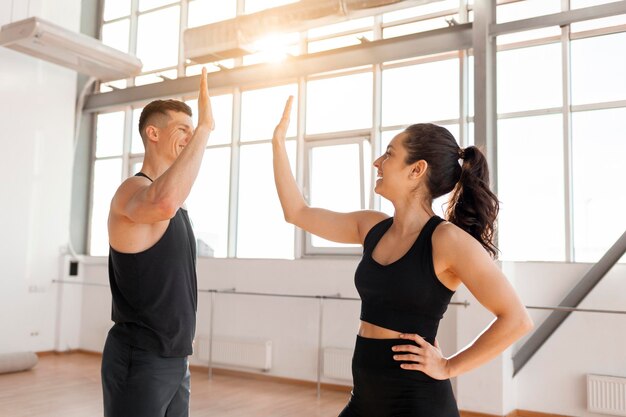 Sportliches Paar in Sportkleidung begrüßt sich im Fitnessstudio. Fitness-Mädchen und Trainer geben ein Highfive.