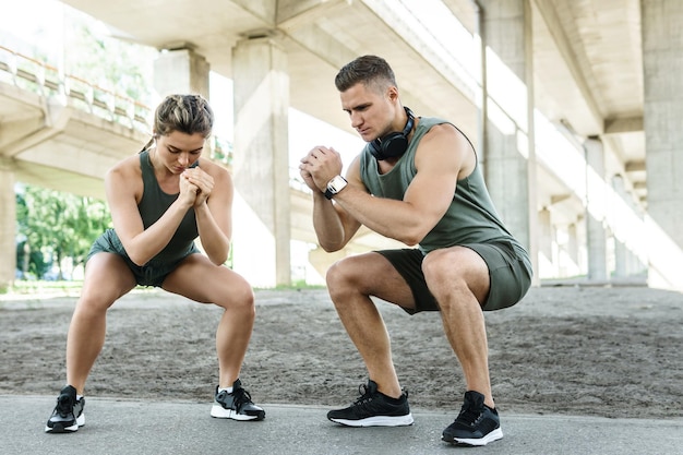 Sportliches Paar und Fitnesstraining im Freien. Mann und Frau machen Kniebeugen während des Straßentrainings.