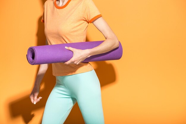 Sportliches Yoga-Mädchen mit Yoga-Matte isoliert über gelb-orangefarbenem Hintergrund