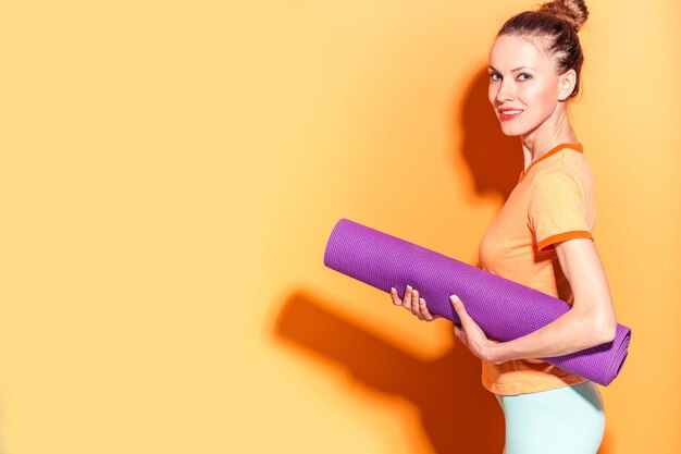 Sportliches Yoga-Mädchen mit Yoga-Matte isoliert über gelb-orangefarbenem Hintergrund