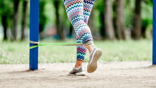 Sportmädchen mit elastischem gummiband beim beintraining im stadion. junge frau, die draußen mit fitnessgeräten trainiert