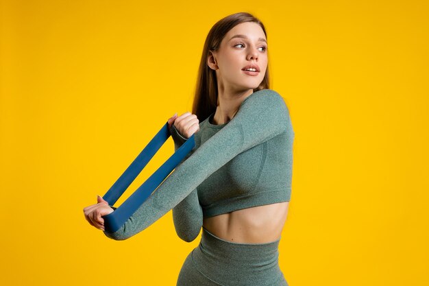 Sportmädchen mit Gummiband für Fitness auf gelbem Hintergrund