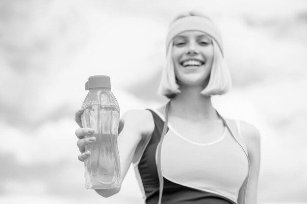 Sportmädchen trinkt Wasser aus einer Flasche auf einem Himmelshintergrund Trinken während des Sports Schwarz und Weiß