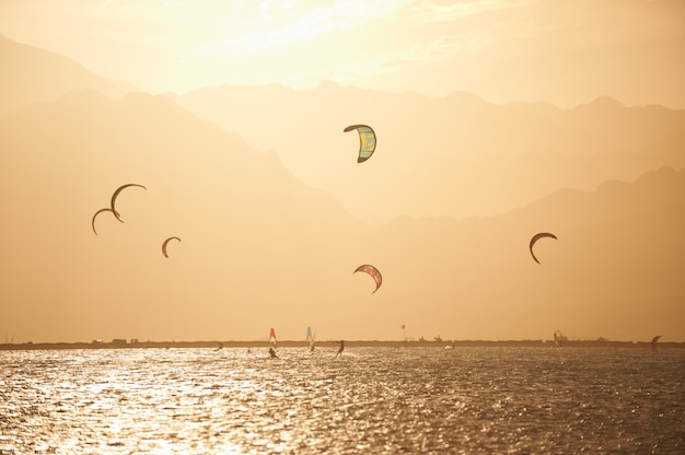Sportmans kitesurf en la superficie del mar contra las montañas al atardecer