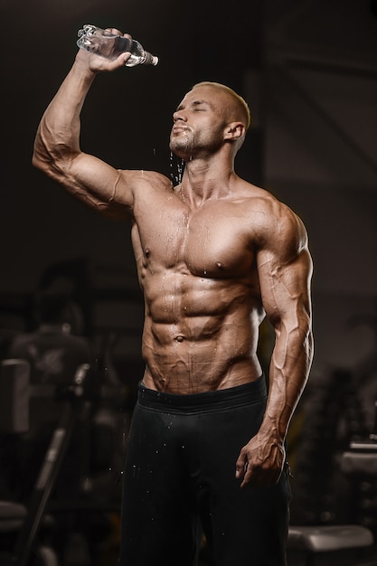 Sportmuskulatur-Fitnessmann-Trinkwasser nach dem Training Cross-Fitness- und Bodybuilding-Konzept Gym abs Muskelübungen im Fitnessstudio nackten Torso Fitness-Konzept