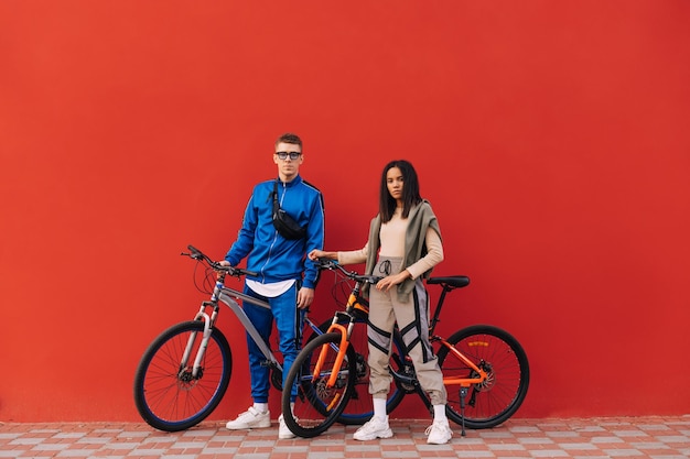 Sportpaare in Sportbekleidung mit Fahrrädern stehen auf dem Hintergrund einer roten Wand