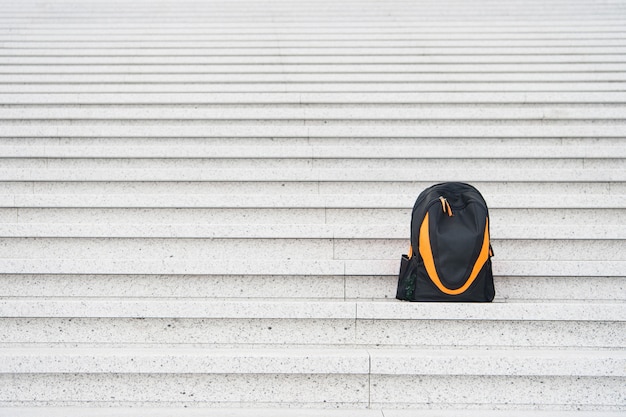 Sporttasche auf der Treppe. Reisen und Urlaub. Schwarzer Rucksack im Freien. Erfolg und Einsamkeit. Schönheit und Mode, Kopienraum