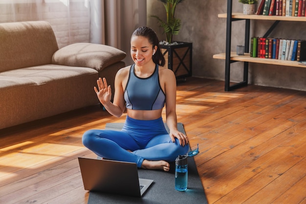 Sporttraining online Junge Frau sitzt auf dem Boden und spricht mit dem Trainer per Laptop