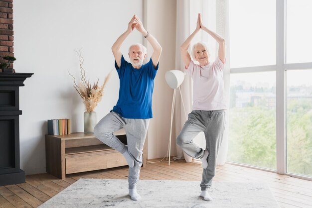 Foto sporty senior anciano pareja de ancianos familia cónyuges abuelos entrenando estiramiento haciendo ejercicios de yoga en casa en el bloqueo juntos manteniendo el equilibrio en un pie