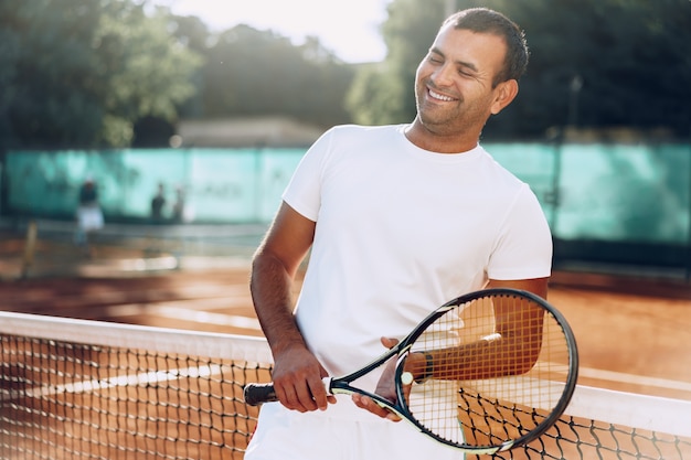 Spoty Mann mit Tennisschläger, der auf Sandtennisplatz nahe Netz steht