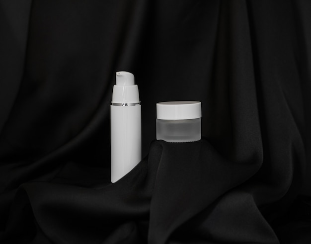 Spray cosmético e frasco cosmético ficam em fundo de seda preta