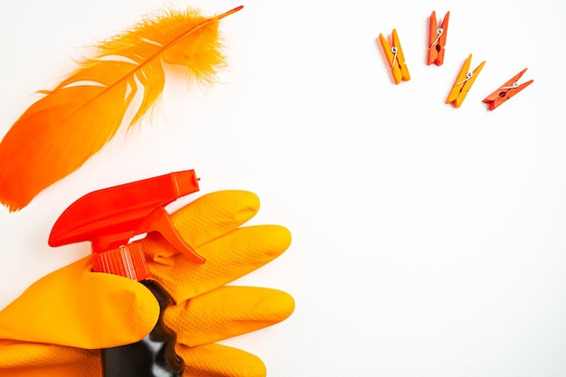 Spray de limpeza preto na mão em luva laranja, prendedores de roupa e pena de laranja na mesa branca