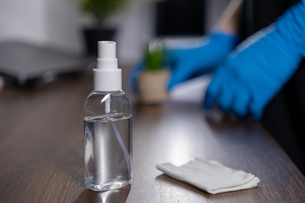 Spray garrafa e pano em superfície de madeira com mãos luvadas limpeza em segundo plano para higiene e desinfecção