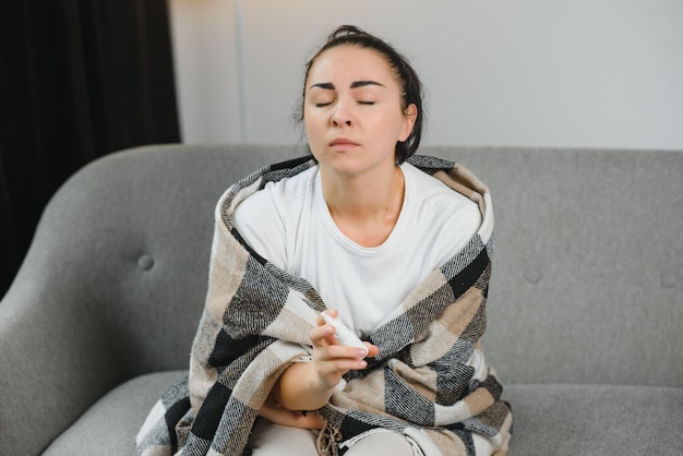 Spray nasal na mão de uma jovem doente sentada no sofá Sintomas e tratamento de rinite alérgica