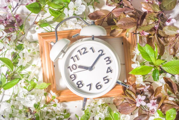 Spring Forward Time Savings Daylight Concept mit Wecker und Frühlingsgartenblumen auf Holzhintergrund Flatlay-Kopienraum auf weißem Holzhintergrund