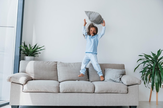 Springen auf dem Sofa Nettes kleines Mädchen drinnen allein zu Hause Kind genießt Wochenende