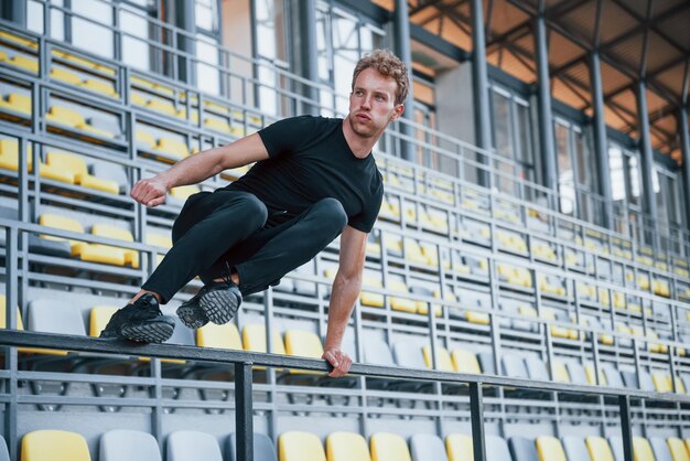 Springen und Parkour auf der Tribüne Sportlicher junger Mann in schwarzem Hemd und Hose tagsüber im Freien