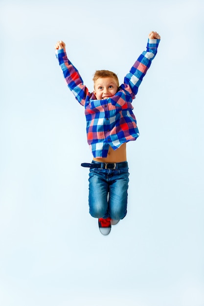 Springender kleiner Junge im bunten karierten Hemd, Blue Jeans, Gummiüberschuhe. Isoliert.