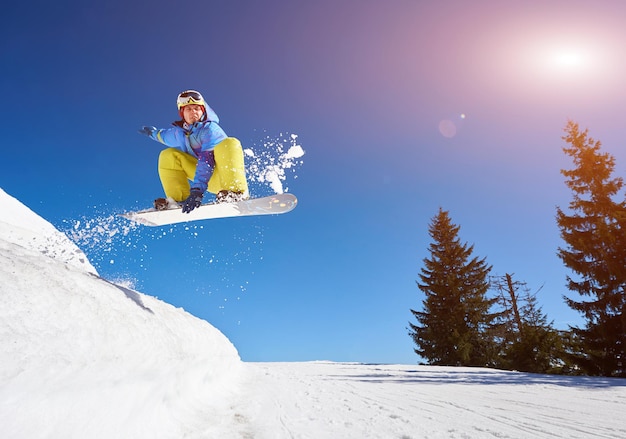 Springender Snowboarder hält eine Hand auf dem Snowboard auf blauem Himmelshintergrund