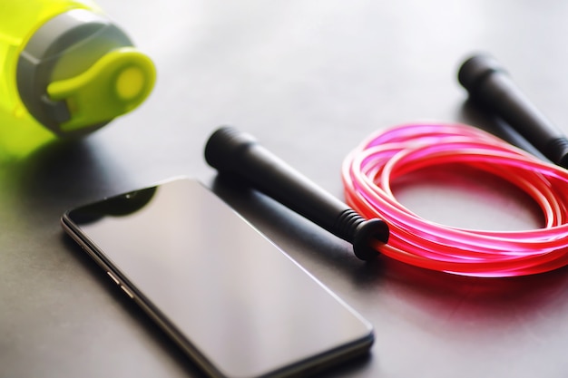 Foto springseil. bewegungserziehung, körpererziehung, leibeserziehung. trainingsgeräte für den sport. seilübungen routine. rosa springseiltelefon mit stoppuhr und wasser auf dem tisch.