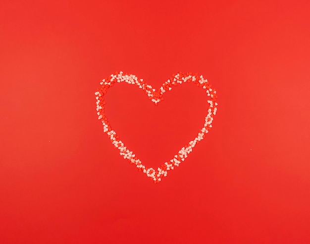 Sprinkles para pasteles en forma de corazón se encuentran sobre un fondo de mesa rojo