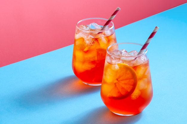 Spritz Cocktail in Gläsern mit Eis und Orangenscheibe auf trendigem buntem Hintergrund