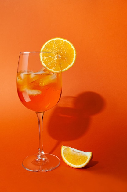 Spritz de aperol de coquetel com gelo Em uma taça de vidro Em um copo de fatia de laranja Ao lado do copo há uma fatia de laranja Em um fundo laranja liso Sombras nítidas de luz dura Closeup Lugar para texto