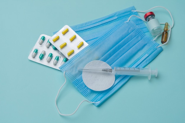 Spritze, Maske, Tabletten, Ampullen auf blauem Hintergrund, Impfkonzept.