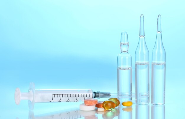 Spritze mit medizinischen Ampullen und Tabletten auf blauem Hintergrund