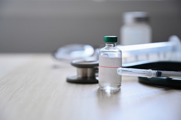 Spritze und Flasche Impfstoff auf Holztisch.