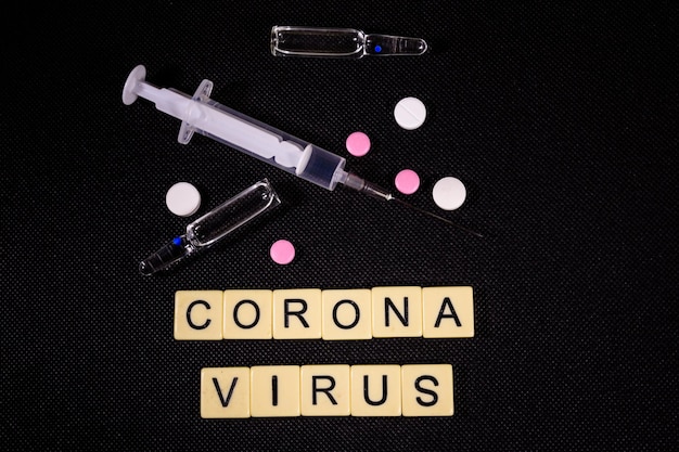 Spritze und Pillen auf schwarzem Hintergrund Gesundheits- und Medizinkonzept Coronavirus-Inschrift