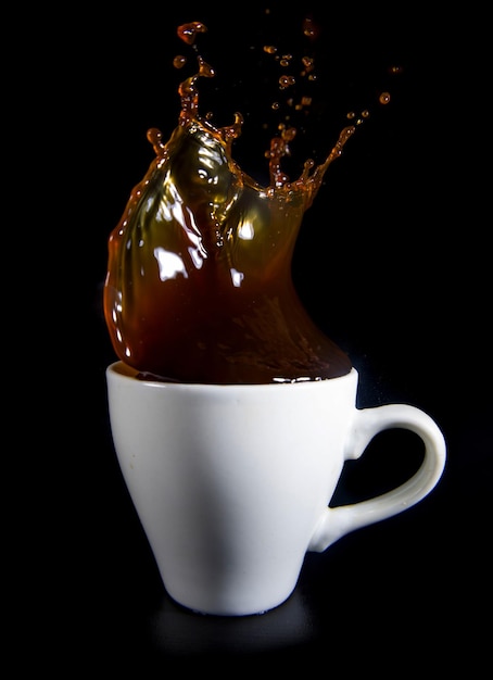 Spritzer Kaffee in einer weißen Tasse auf schwarzem Hintergrund