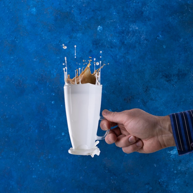 Spritzer Milch in einem Glas schweben auf blauem Hintergrund mit einer Hand